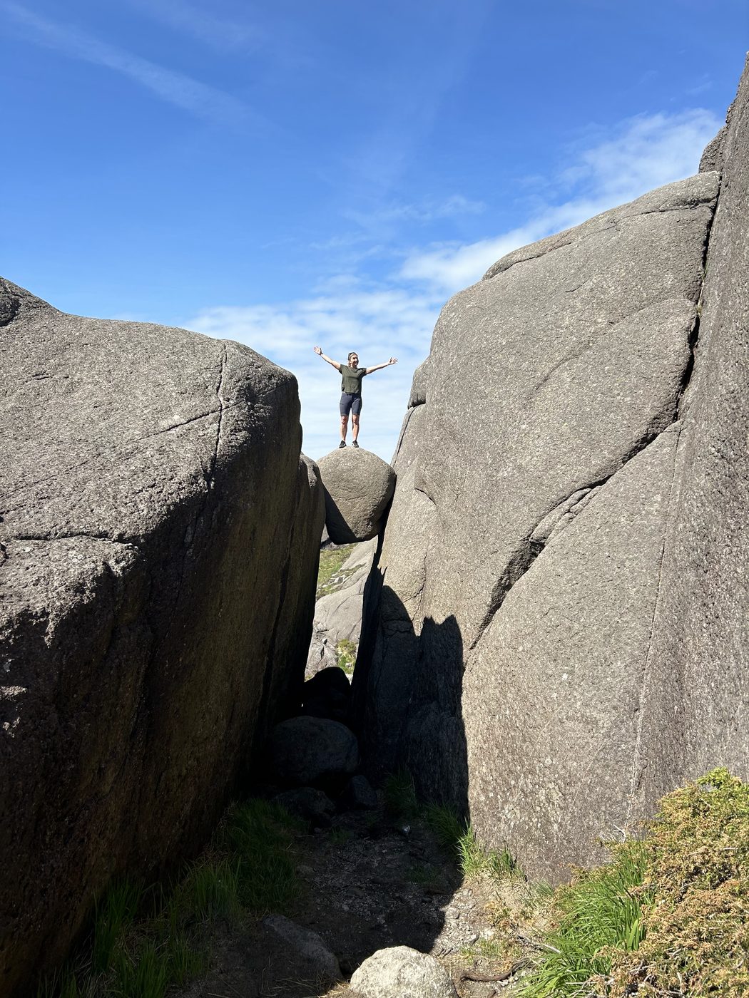 A hiker standing with arms raised on a boulder wedged between two large rock faces