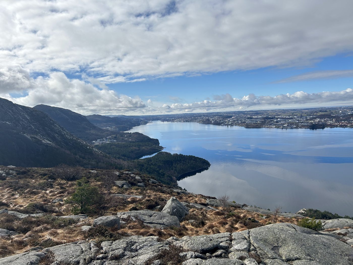 A sweeping view from a rocky summit over a calm fjord and a coastal town