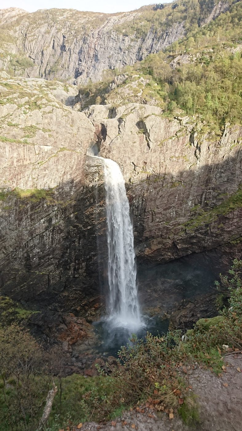 A tall waterfall dropping into a pool in a mountain gorge